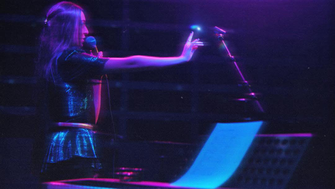 Isabelle Henderson performing under blue and pink lighting.